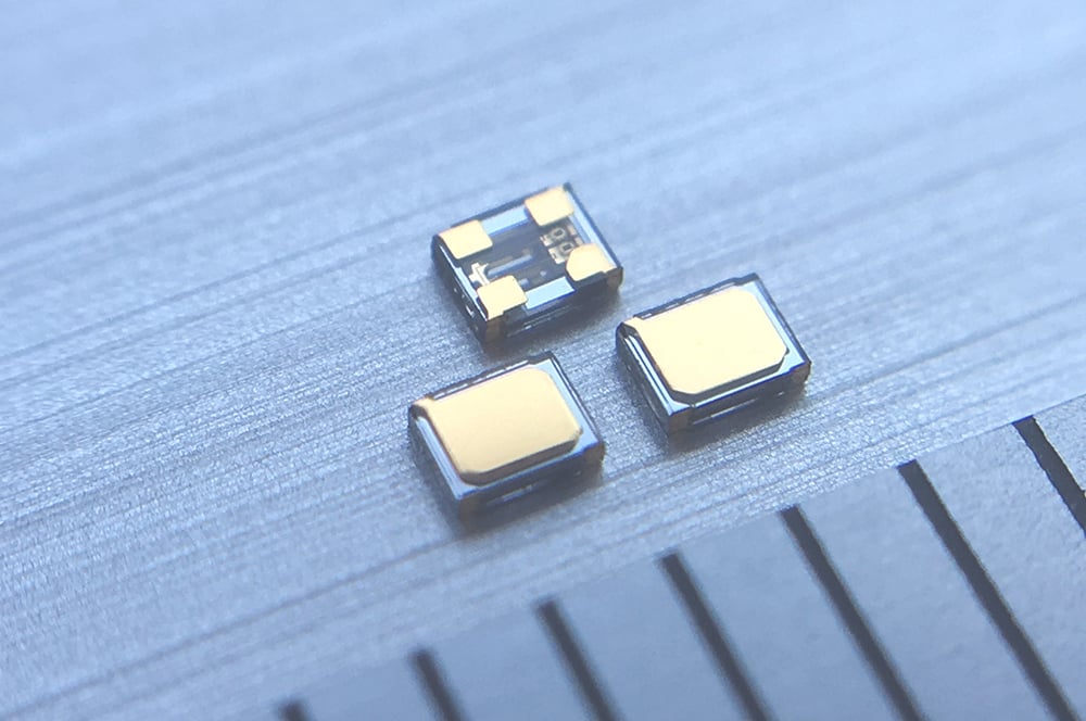 Three TFX-05X 1210-size ultra-small tuning fork crystal units alongside a ruler for scale, as detailed in the reliability report by River Eletec, the world's No.1 provider of miniature crystal units.